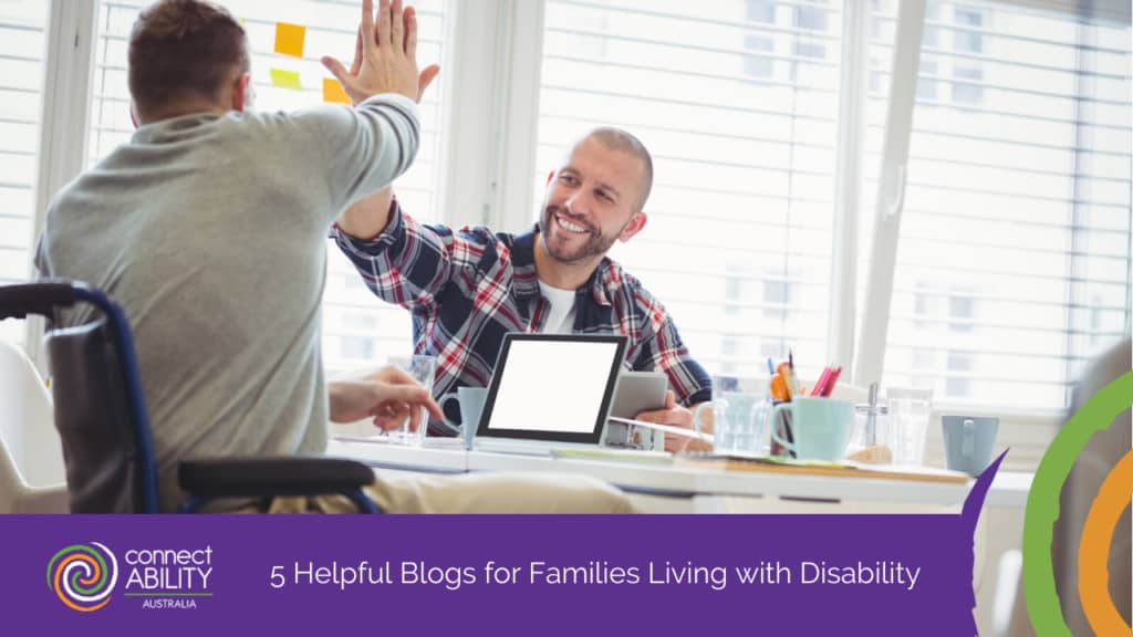 Two men, one in a wheelchair, share a high-five at a desk in a bright office