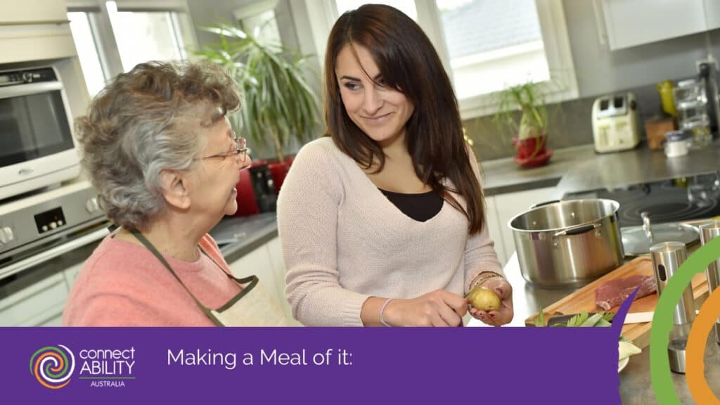 A younger woman smiling as she helps an older woman in an apron peel a potato in a kitchen