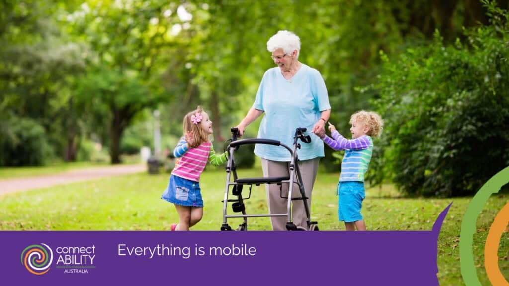 An elderly woman using a walker and smiling at two young children in a lush green park