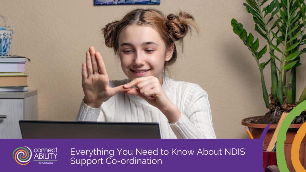 A young woman with her hair in buns smiling while using sign language in front of a laptop