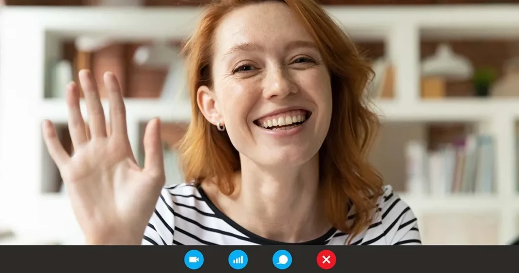 A smiling redhead woman waves during a video call.