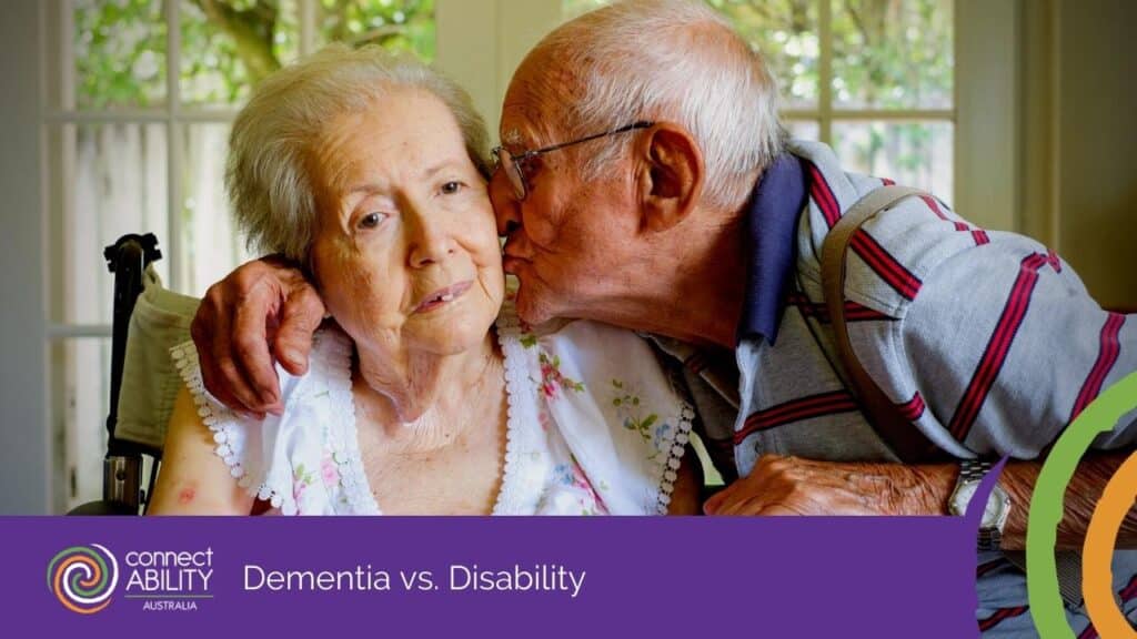 An elderly man kissing an elderly woman in a wheelchair on the cheek