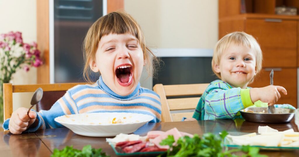 Two young children sitting at a dining table with plates of food
