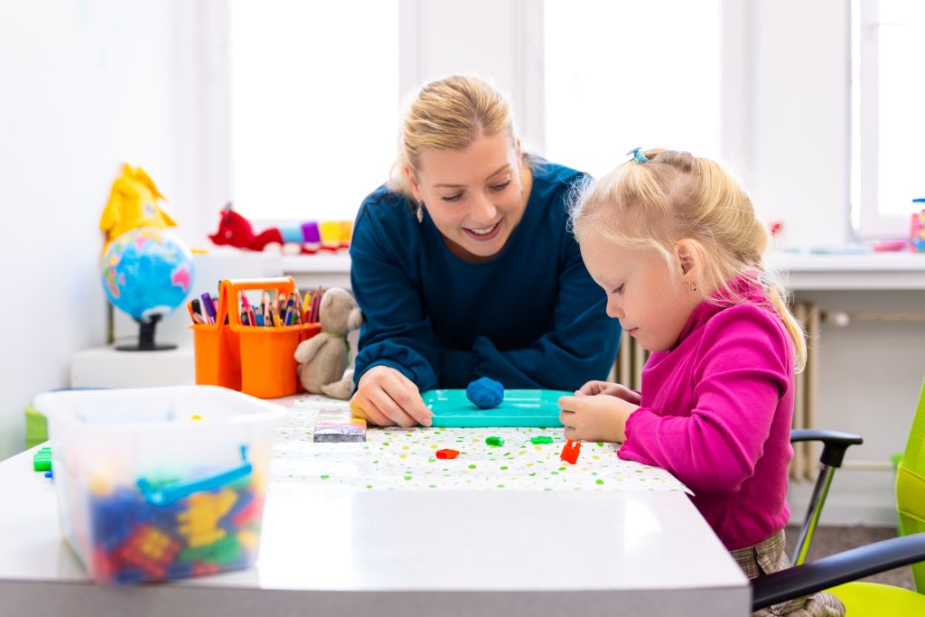 A woman in a dark blue sweater and a young girl in a pink shirt who is focused on playing with small colourful toys