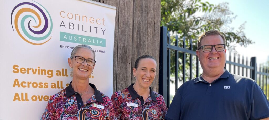 Three people smiling while standing in front of a ConnectAbility Australia banner.